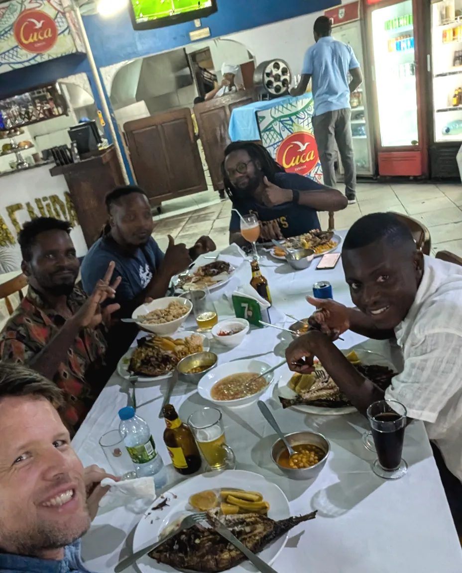 Reporters and local crew sharing a long table of food after a shoot in Luanda